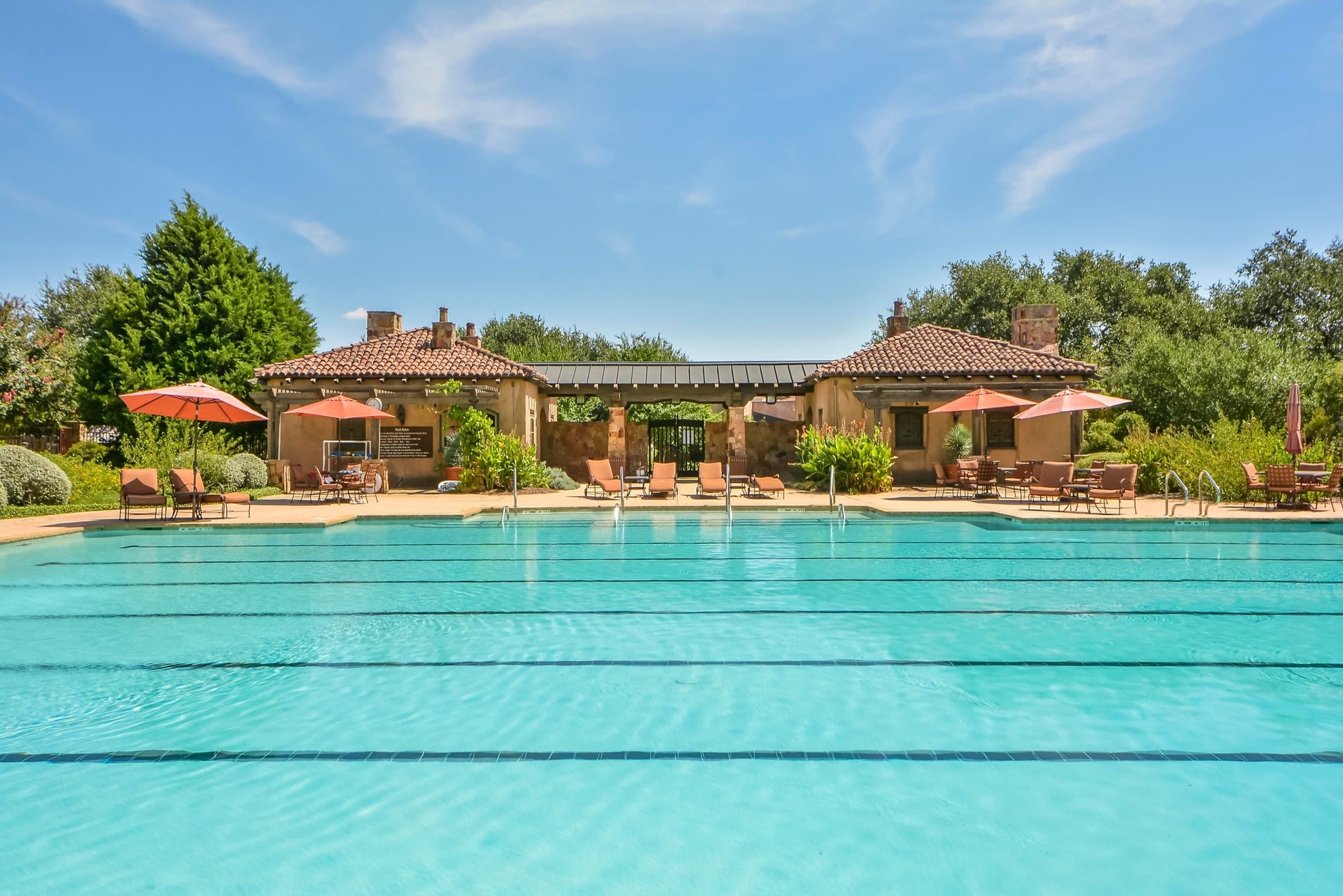 Resort-style lap pool with terracotta tile roof clubhouse and orange umbrellas