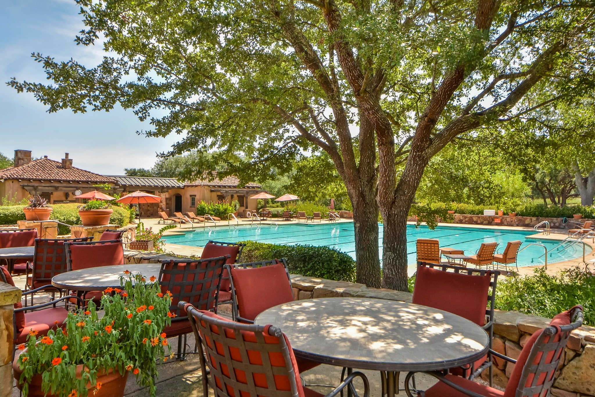 Pool terrace dining area with red chairs, round tables, and mature oak tree