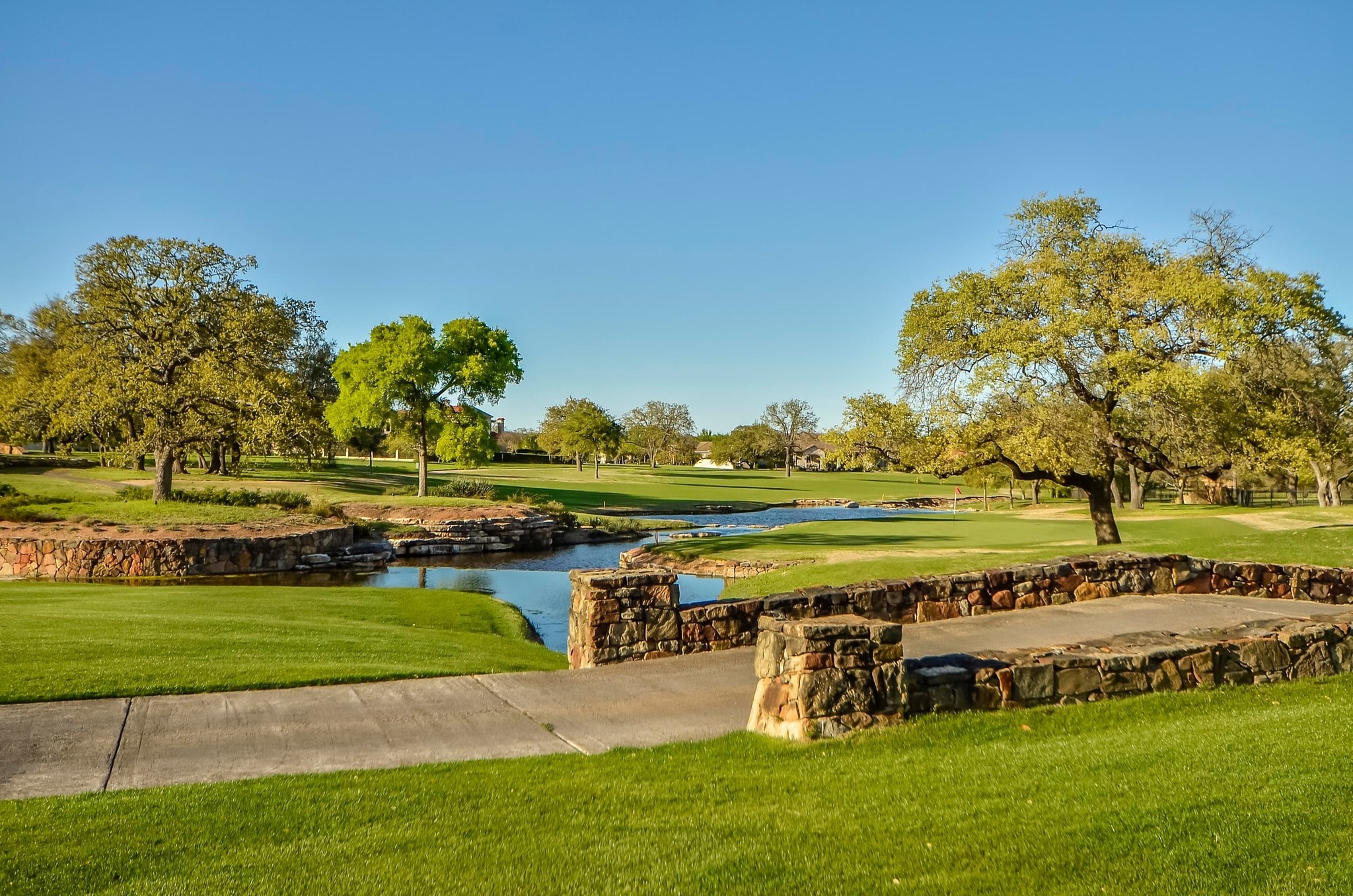Golf course fairway with stone-lined creek, bridge, and Hill Country oaks