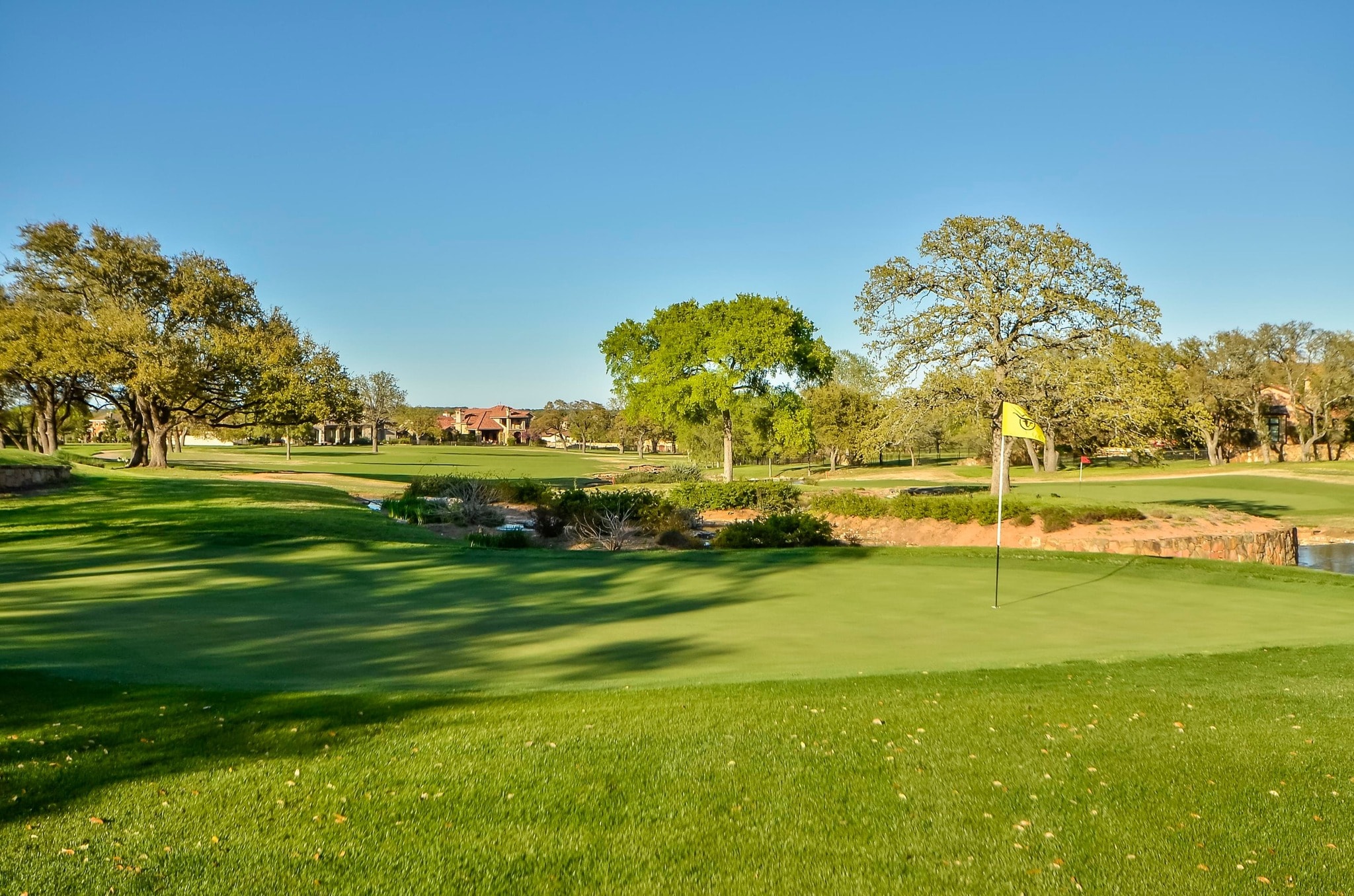 Golf course fairway with yellow flag and Hill Country homes in background